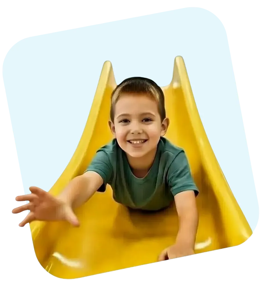 Nasmejani dečak se spu&scaron;ta niz žuti tobogan u igraonici